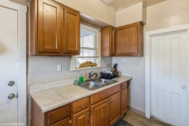 kitchen featuring a sink, baseboards, brown cabinetry, and light countertops