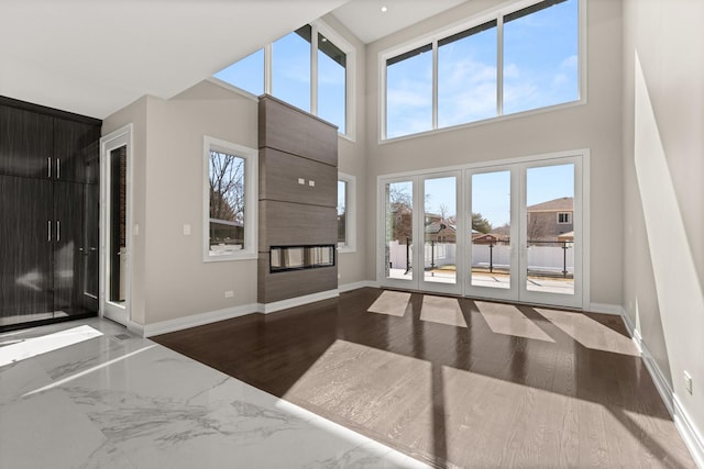 foyer featuring baseboards, a high ceiling, and a large fireplace