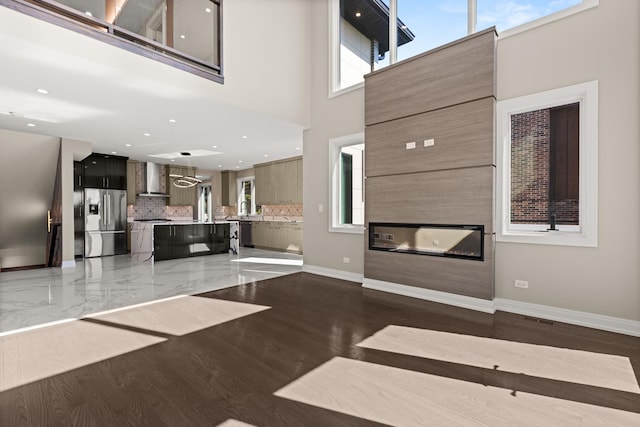 unfurnished living room featuring a glass covered fireplace, a towering ceiling, baseboards, recessed lighting, and light wood finished floors