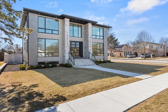 contemporary house with fence, a residential view, a front lawn, and brick siding