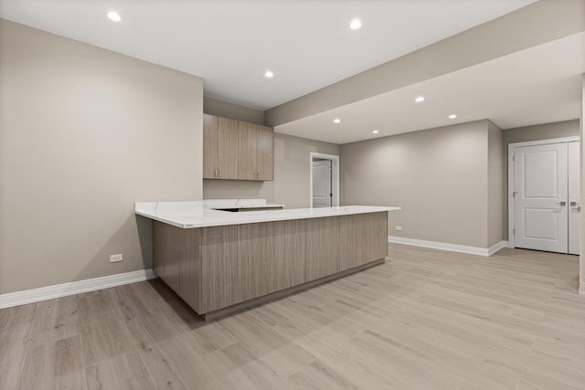 kitchen with baseboards, a peninsula, light brown cabinetry, and light wood-type flooring
