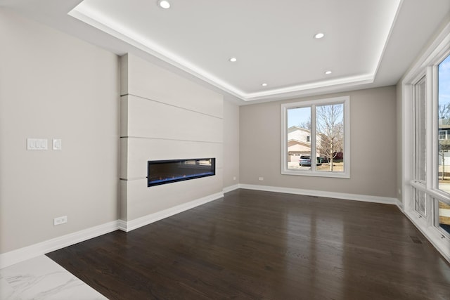 unfurnished living room featuring recessed lighting, baseboards, a glass covered fireplace, and a tray ceiling