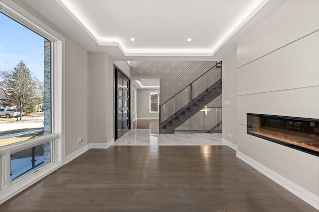 unfurnished living room with a glass covered fireplace, recessed lighting, baseboards, wood finished floors, and stairway