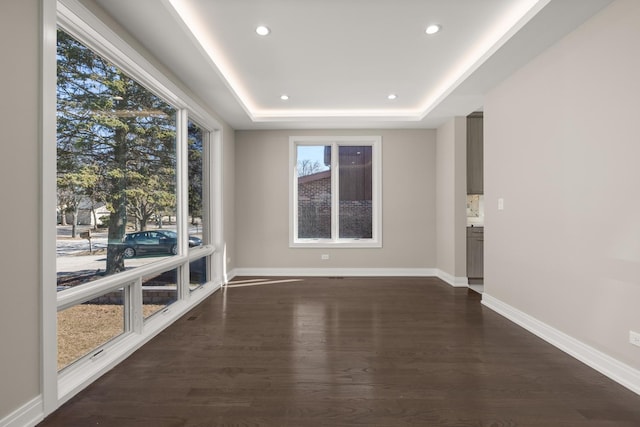 spare room with baseboards, a tray ceiling, and dark wood-style floors