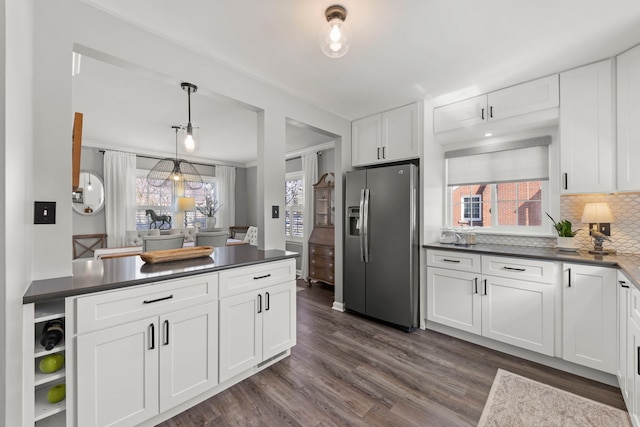 kitchen with stainless steel refrigerator with ice dispenser, dark countertops, dark wood finished floors, white cabinets, and decorative backsplash