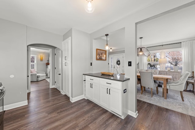 kitchen featuring dark countertops, baseboards, dark wood finished floors, arched walkways, and white cabinetry