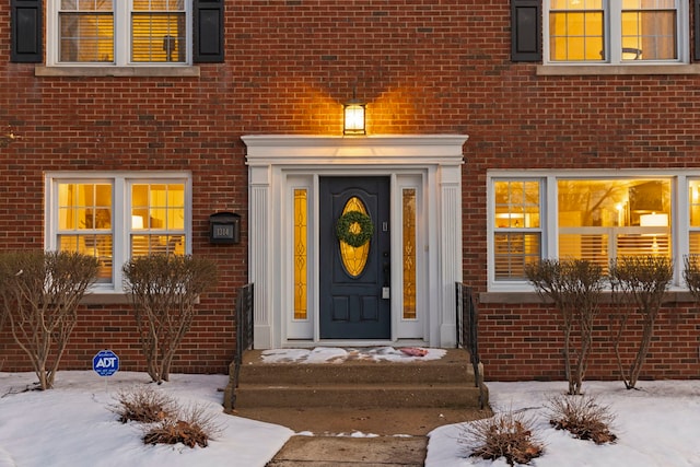 snow covered property entrance featuring brick siding