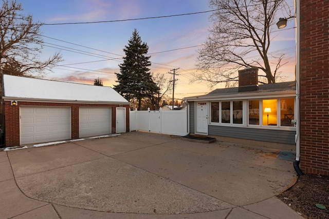 garage at dusk featuring fence and a garage
