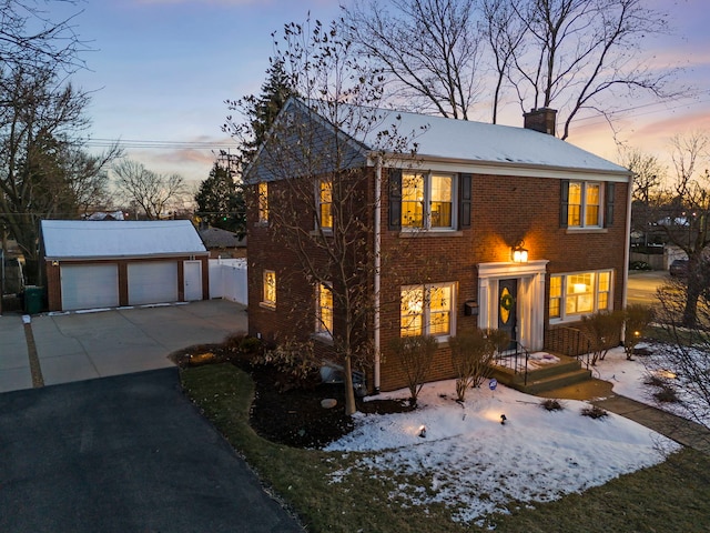 colonial home featuring brick siding, a chimney, a detached garage, and an outdoor structure