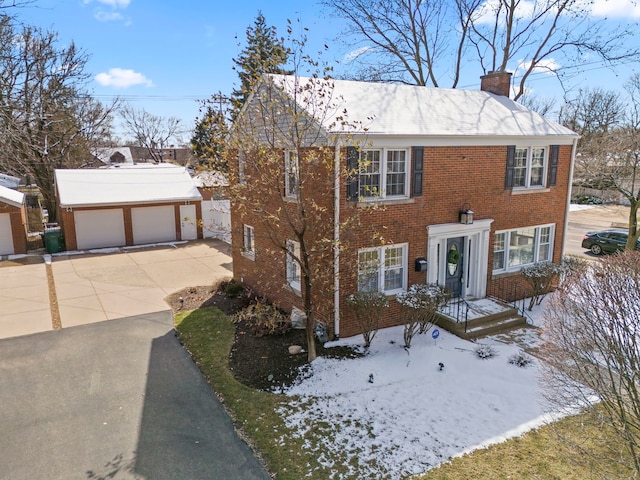 colonial house featuring an outbuilding, driveway, a garage, brick siding, and a chimney