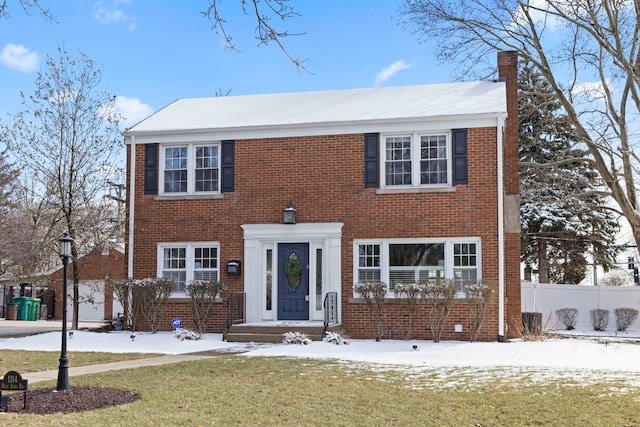 colonial house featuring a lawn, fence, brick siding, and a chimney