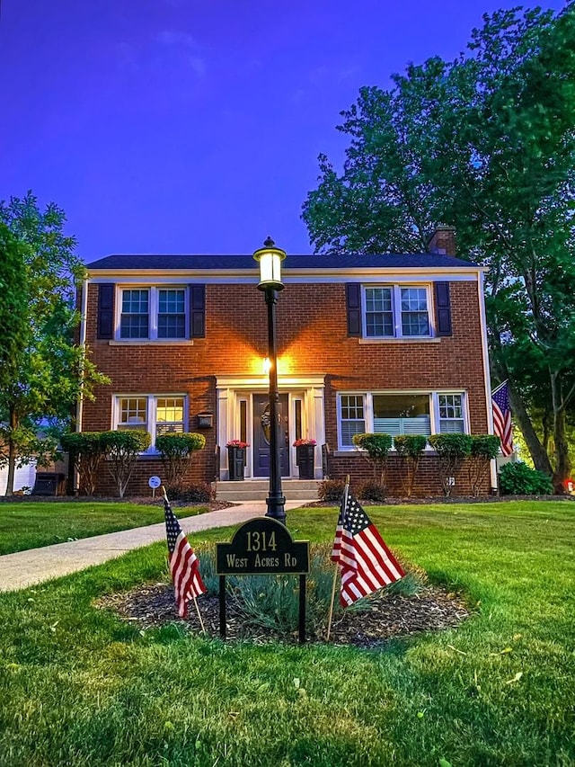 view of front facade featuring a front lawn, brick siding, and a chimney