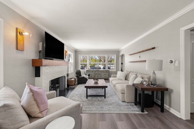 living room featuring wood finished floors, arched walkways, a fireplace, crown molding, and baseboards