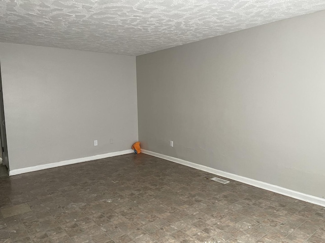 empty room with dark floors, visible vents, and baseboards