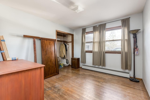 unfurnished bedroom featuring a baseboard heating unit, a closet, and light wood finished floors