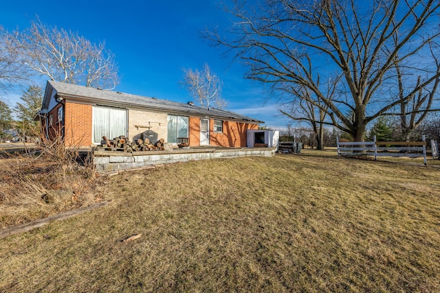 back of house featuring brick siding, a lawn, and fence