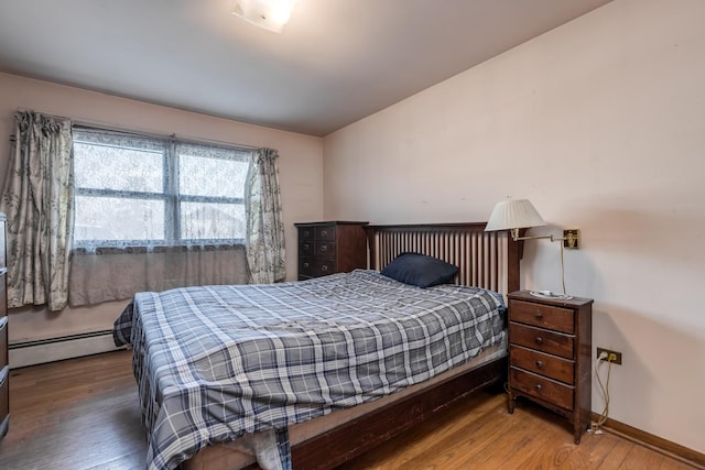 bedroom featuring a baseboard heating unit, wood finished floors, and baseboards