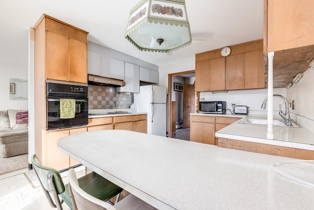 kitchen featuring oven, under cabinet range hood, stainless steel microwave, a sink, and freestanding refrigerator