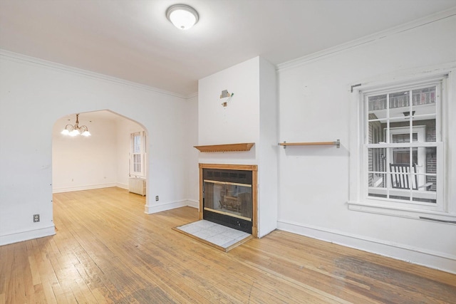 unfurnished living room featuring hardwood / wood-style floors, baseboards, arched walkways, a glass covered fireplace, and crown molding