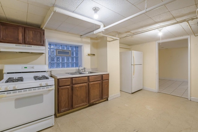 kitchen with white appliances, brown cabinetry, light floors, a sink, and under cabinet range hood