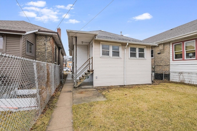 rear view of house featuring entry steps, a yard, and fence