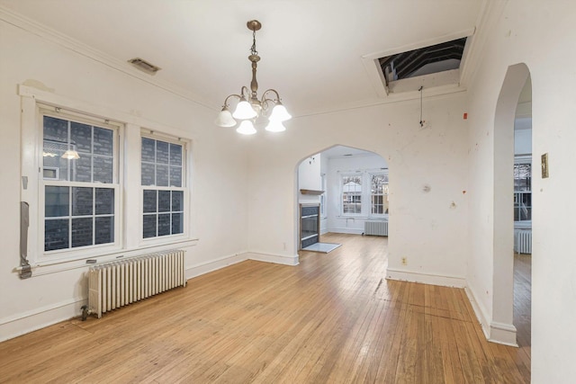 unfurnished dining area featuring arched walkways, visible vents, light wood finished floors, and radiator heating unit