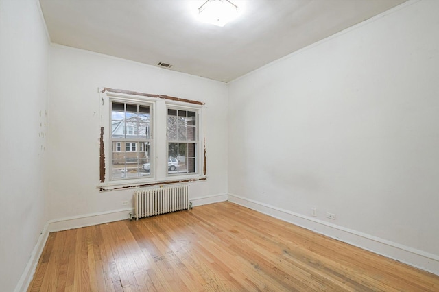 empty room featuring visible vents, wood-type flooring, radiator, crown molding, and baseboards