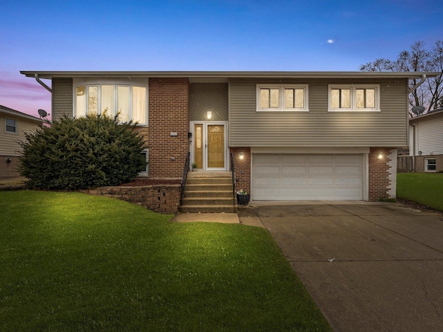 raised ranch with a garage, a yard, brick siding, and driveway