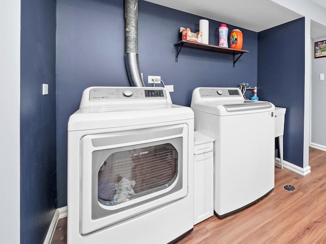 clothes washing area with laundry area, baseboards, light wood finished floors, and washing machine and clothes dryer