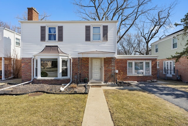 traditional-style house featuring brick siding, a chimney, a front yard, and fence