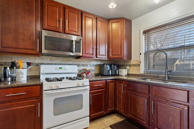 kitchen with light tile patterned floors, a sink, decorative backsplash, white gas range oven, and stainless steel microwave