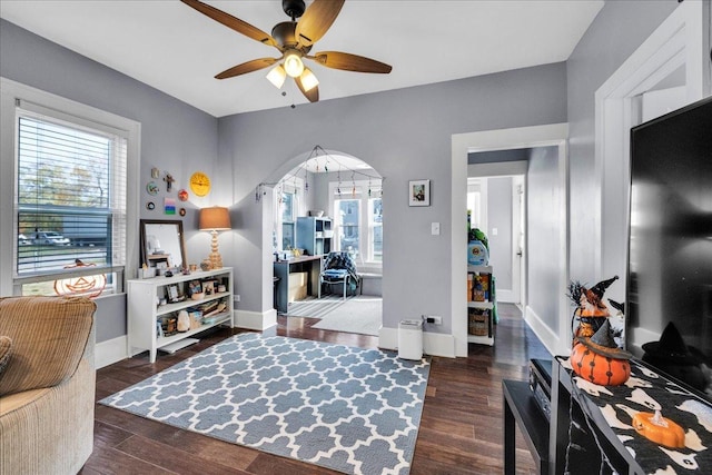 interior space with baseboards, arched walkways, wood finished floors, and a ceiling fan