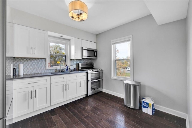 kitchen with a sink, dark countertops, tasteful backsplash, appliances with stainless steel finishes, and baseboards