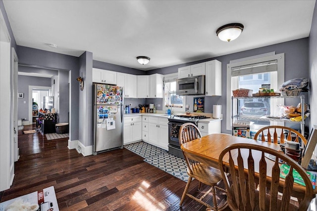 kitchen featuring white cabinetry, appliances with stainless steel finishes, light countertops, baseboards, and dark wood-style flooring