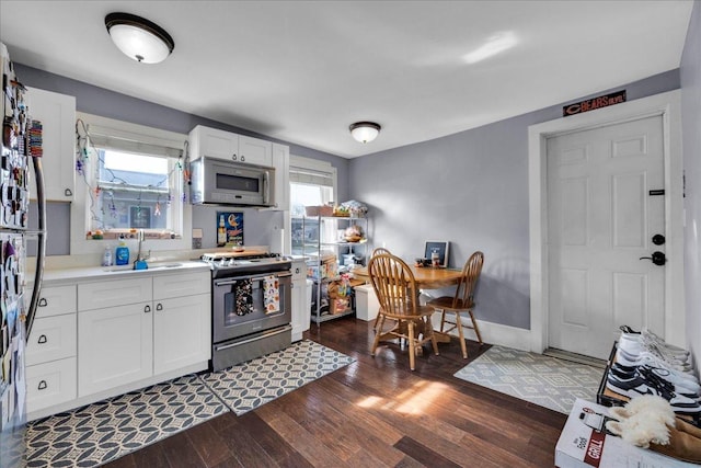 kitchen featuring a sink, dark wood finished floors, light countertops, white microwave, and stainless steel range with gas stovetop