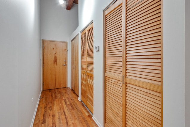 hall featuring light wood-style floors, baseboards, and a towering ceiling