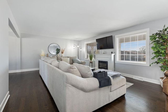 living room with a glass covered fireplace, visible vents, baseboards, and dark wood-style floors