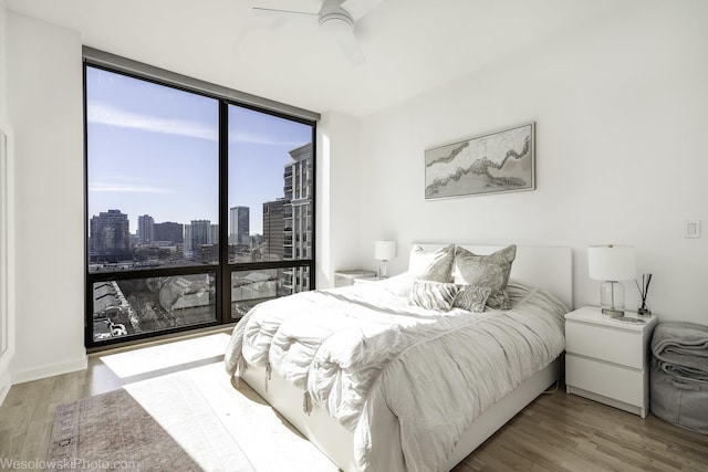 bedroom with a city view, wood finished floors, ceiling fan, and expansive windows