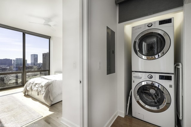 washroom featuring wood finished floors, laundry area, electric panel, stacked washer and clothes dryer, and a city view