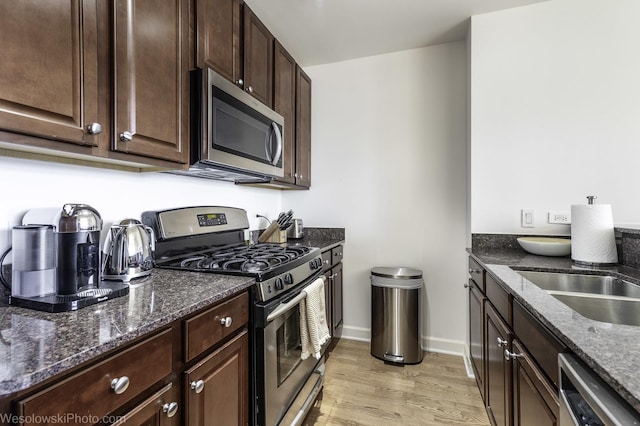 kitchen with dark stone countertops, baseboards, light wood-style flooring, stainless steel appliances, and dark brown cabinetry