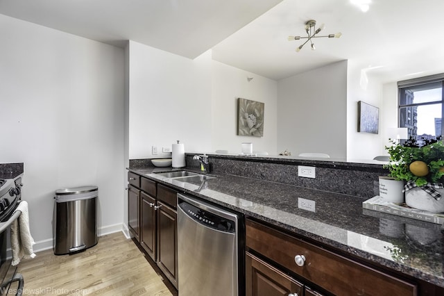 kitchen with light wood finished floors, a sink, dishwasher, dark stone countertops, and range