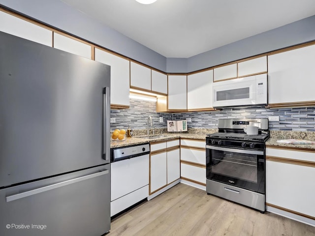 kitchen with a sink, light wood-type flooring, appliances with stainless steel finishes, and white cabinetry