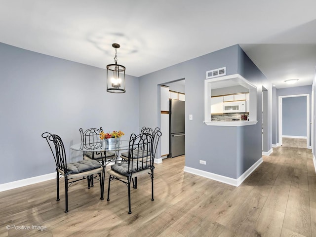 dining space featuring baseboards, wood finished floors, visible vents, and a chandelier