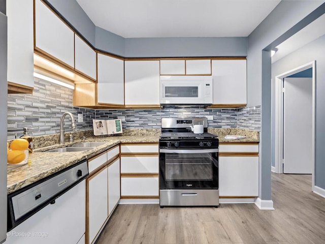 kitchen with a sink, white appliances, light wood-style floors, and white cabinets