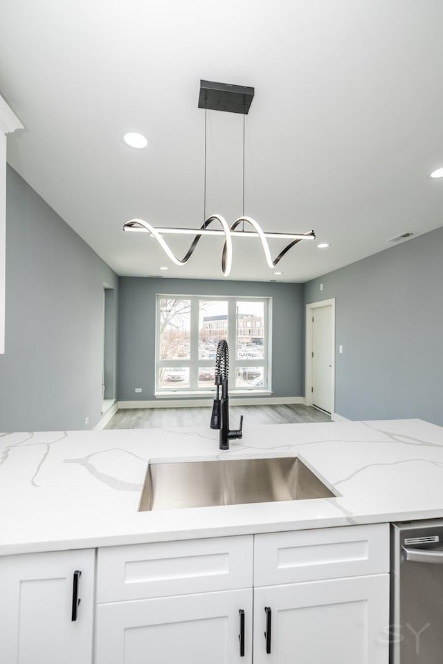 kitchen with light stone counters, visible vents, a sink, white cabinets, and decorative light fixtures