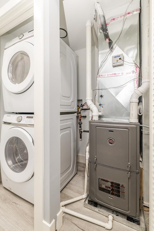 laundry room with laundry area, heating unit, wood finished floors, and stacked washer and clothes dryer