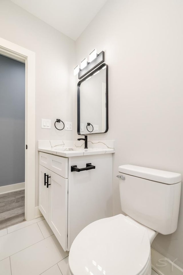 half bathroom featuring tile patterned floors, baseboards, toilet, and vanity