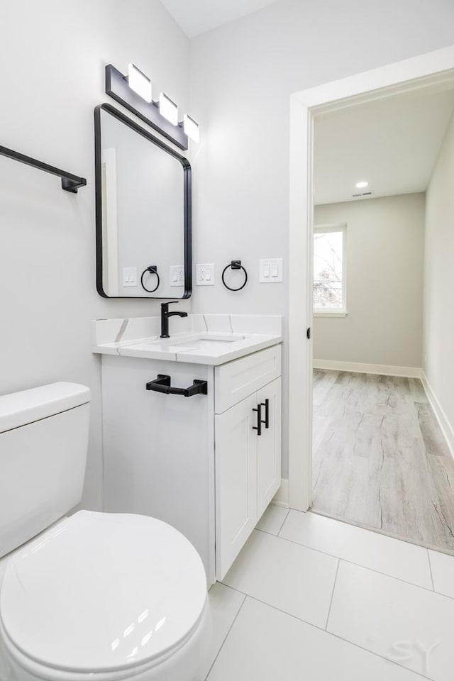 half bath with baseboards, toilet, vanity, and tile patterned flooring