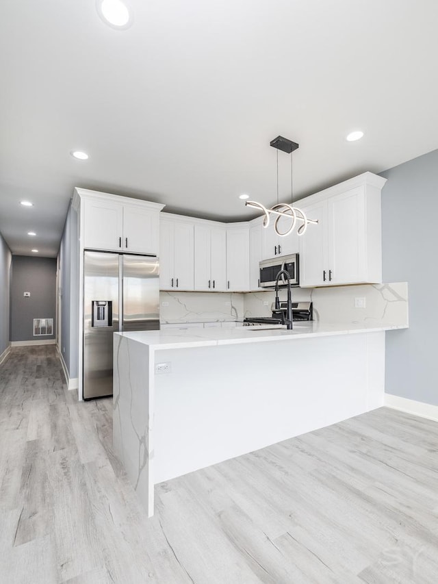 kitchen with decorative light fixtures, light countertops, light wood-style flooring, stainless steel appliances, and white cabinetry