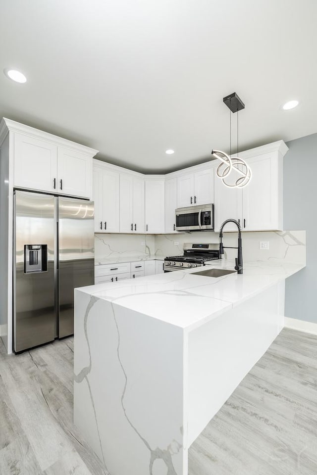 kitchen featuring light wood finished floors, light stone counters, appliances with stainless steel finishes, a peninsula, and white cabinetry